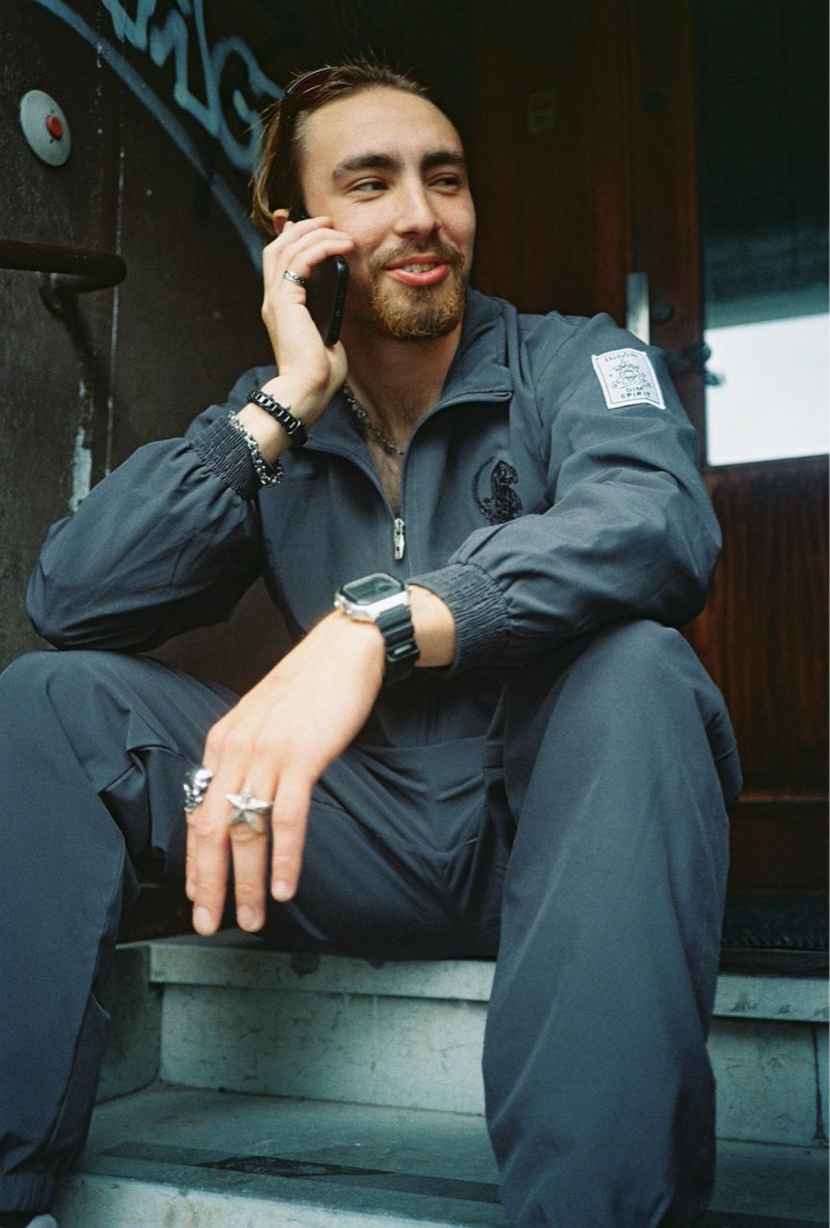 Model wearing the Dim Spirit x WebZero windbreaker tracksuit, seated on steps
